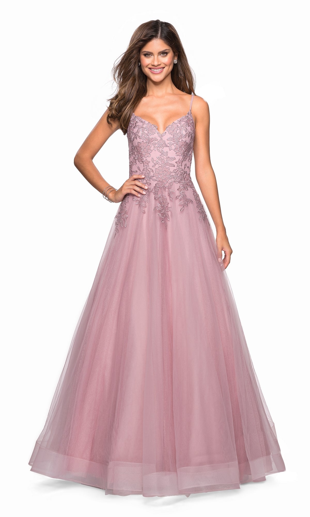 A woman stands smiling with one hand on her hip, wearing the La Femme 27569 Cut-Out Embroidered Tulle Prom Dress— a sleeveless, floor-length mauve gown with a lace bodice, tulle skirt, and delicate floral embroidery.